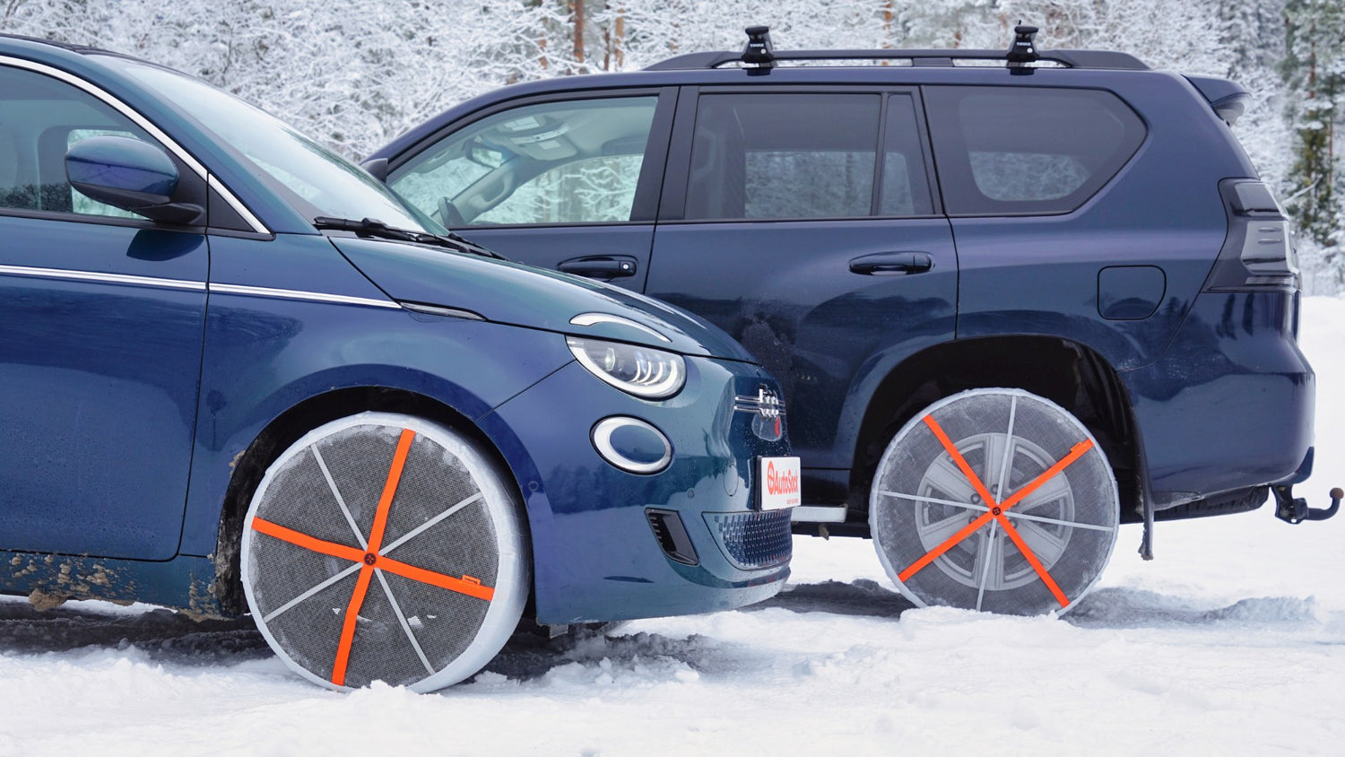 Front view of textile snow chains mounted on the front tires of Fiat 500 and rear wheels of Toyota off-road vehicle